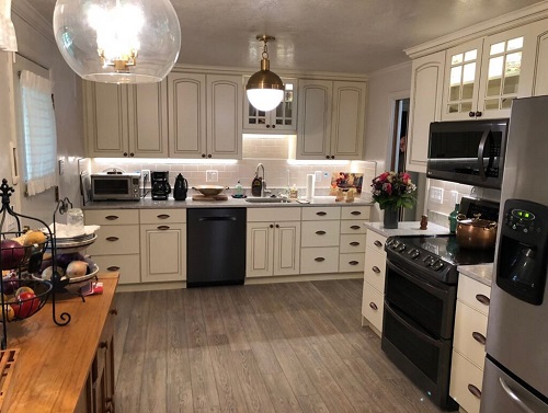 A newly remodeled kitchen features white cabinets, vinyl flooring, and pendant lighting.